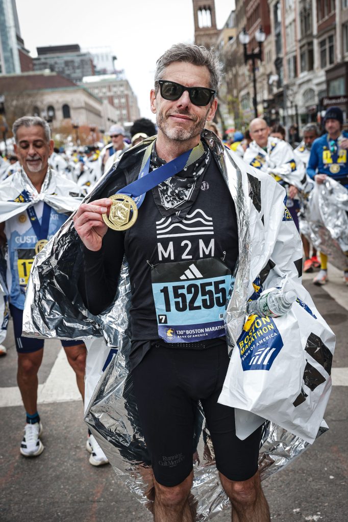 Me at the Boston Marathon finish, holding my medal, wrapped in a Boston Marathon heat sheet.